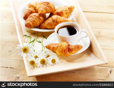 coffee and croissants with daisy flowers on wooden tray