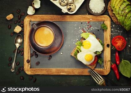 Coffee and sandwich(fried eggs, avocado, tomatoes) on rustic background, top view