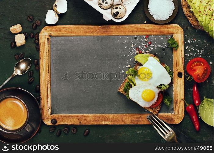 Coffee and sandwich(fried eggs, avocado, tomatoes) on rustic background, top view