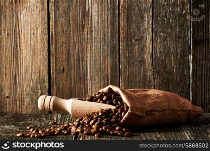 Coffee beans and scoop in sack on wooden table