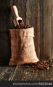 Coffee beans and scoop in sack on wooden table