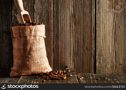 Coffee beans and scoop in sack on wooden table