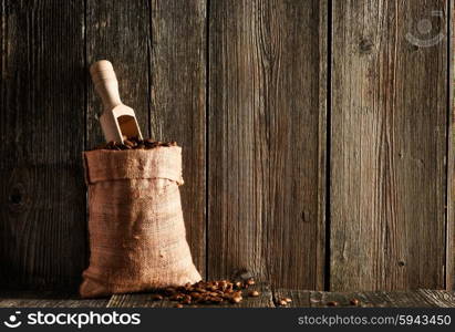 Coffee beans and scoop in sack on wooden table