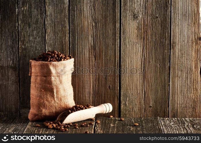 Coffee beans and scoop in sack on wooden table