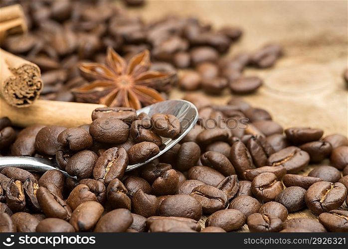 Coffee beans and spoon with cinnamon sticks and star anise on wooden background