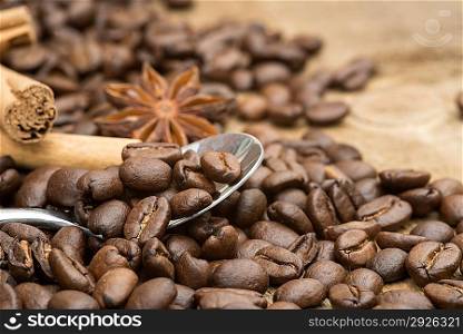 Coffee beans and spoon with cinnamon sticks and star anise on wooden background