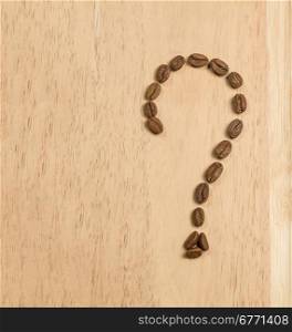 Coffee beans are laid out on a wooden board in the form of a question mark, studio shot