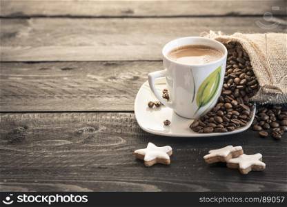 Coffee beans coming out from a small burlap sack and cup of hot coffee on a rustic black wooden table