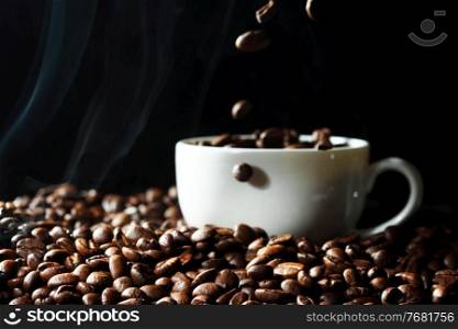 Coffee beans falling in black coffee cup, black background. Cup with coffee beans
