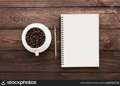 coffee beans in cup and book blank page on wood table