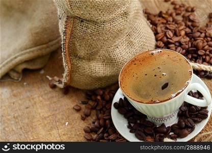 coffee beans in jute sack behind cup of black coffee