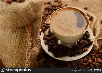 coffee beans in jute sack behind cup of black coffee