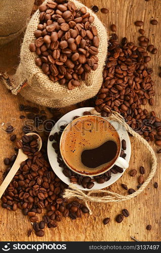 coffee beans in jute sack behind cup of black coffee