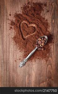 Coffee beans in metal spoon and coffee powder with heart shape on wooden background. Coffee beans in metal spoon and coffee powder with heart shape