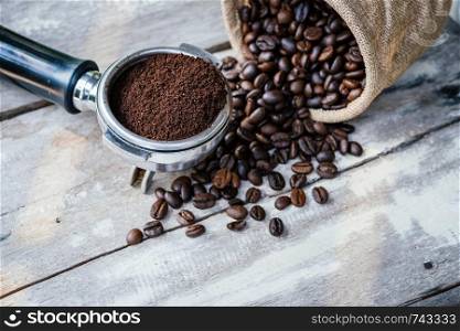 Coffee beans in sack and portafilter on old white wooden table background.