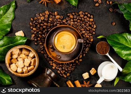 Coffee beans in shape of heart, cup of coffee, milk and sugar on dark rustic background flat lay. Creative flat lay with coffee, milk and sugar