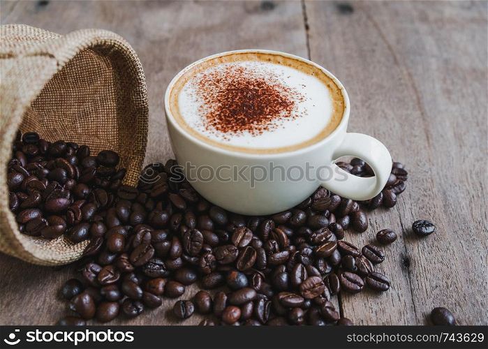 Coffee beans in the sack with a coffee cup on wooden table background.
