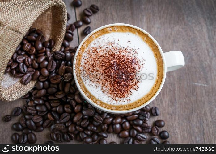 Coffee beans in the sack with a coffee cup on wooden table background.