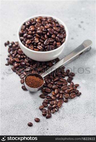Coffee beans in white ceramic bowl with steel coffee soop on light table background.