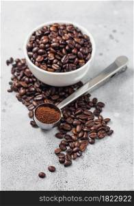 Coffee beans in white ceramic bowl with steel coffee soop on light table background.