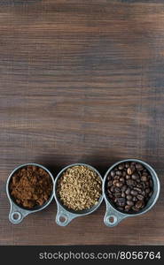 Coffee beans, instant coffee and ground coffee in a metal measuring cup on dark wooden background with copy-space, top view