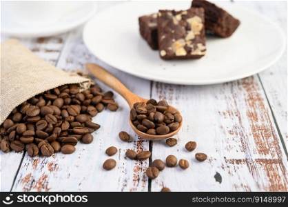 Coffee beans on wooden spoon and hemp sacks on a white wood table.