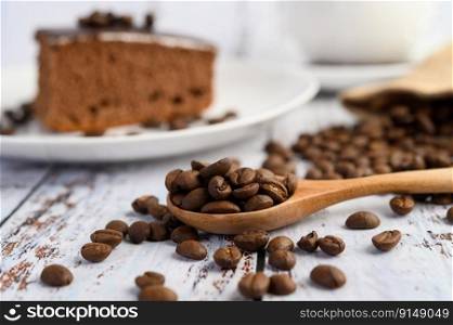 Coffee beans on wooden spoon on a white wood table.