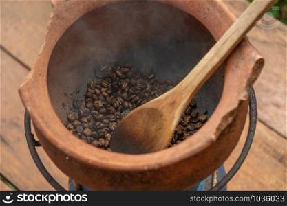 Coffee beans that are roasted on a clay pot whit wooden turner. Soft focus