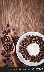 Coffee beans with wooden scoop and saucer on wooden background. Coffee beans with wooden scoop and saucer