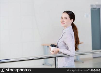 Coffee break. Casual caucasian woman standing at balcony with coffee in hands
