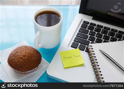Coffee break, cupcake and notebook place on laptop with sticky note message : Break Time, A break at work concept