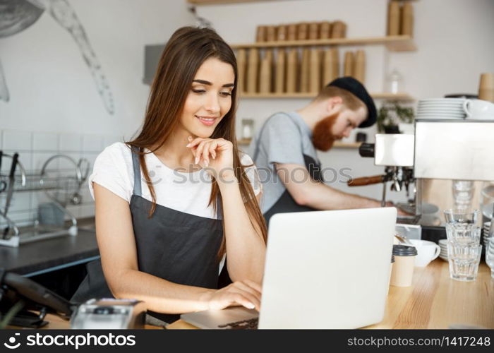 Coffee Business Concept - beautiful caucasian bartender barista or manager working and planing in laptop at modern coffee shop.