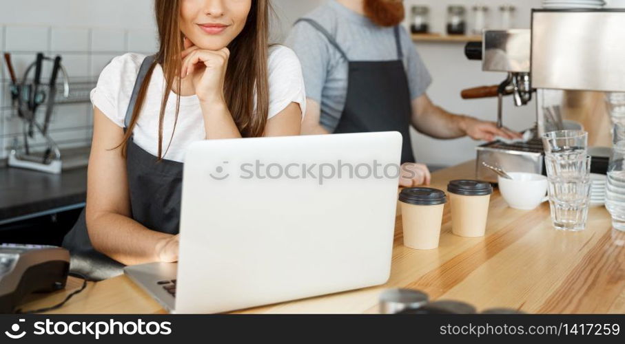 Coffee Business Concept - beautiful caucasian bartender barista or manager working and planing in laptop at modern coffee shop.