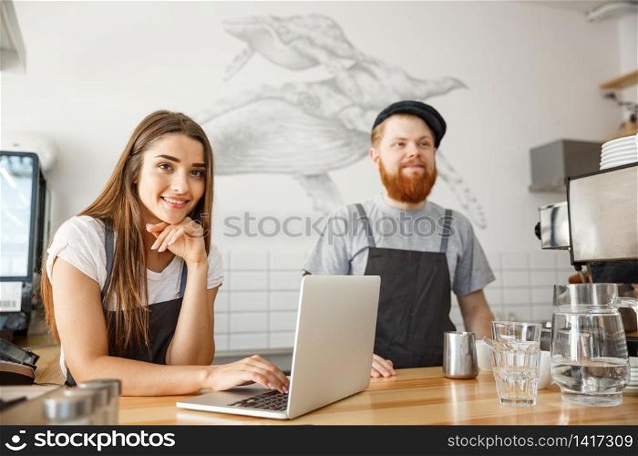 Coffee Business Concept - Cheerful baristas looking at their laptop for online orders in modern coffee shop.