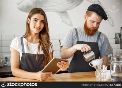 Coffee Business Concept - Cheerful baristas looking at their tablets for online orders in modern coffee shop.