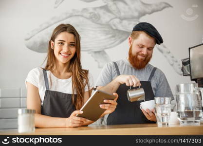 Coffee Business Concept - Cheerful baristas looking at their tablets for online orders in modern coffee shop.