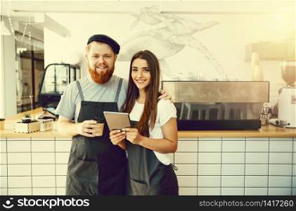 Coffee Business Concept - Cheerful baristas looking at their tablets for online orders. Coffee Business Concept - Cheerful baristas looking at their tablets for online orders.