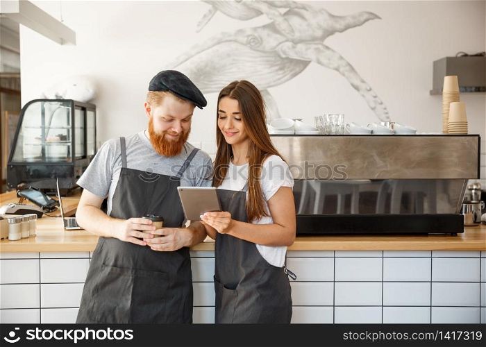 Coffee Business Concept - Cheerful baristas looking at their tablets for online orders.