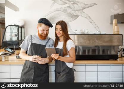 Coffee Business Concept - Cheerful baristas looking at their tablets for online orders.