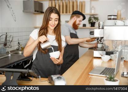 Coffee Business Concept - close-up lady barista in apron preparing and pouring milk into hot cup while standing at cafe.