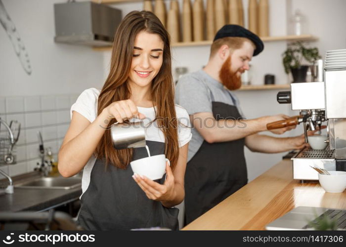 Coffee Business Concept - close-up lady barista in apron preparing and pouring milk into hot cup while standing at cafe.