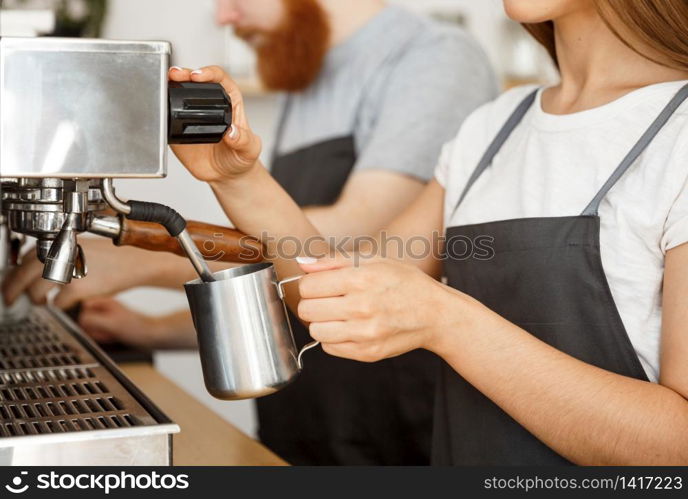 Coffee Business Concept - portrait of lady barista in apron preparing and steaming milk for coffee order with her partner while standing at cafe.