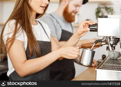Coffee Business Concept - portrait of lady barista in apron preparing and steaming milk for coffee order with her partner while standing at cafe.