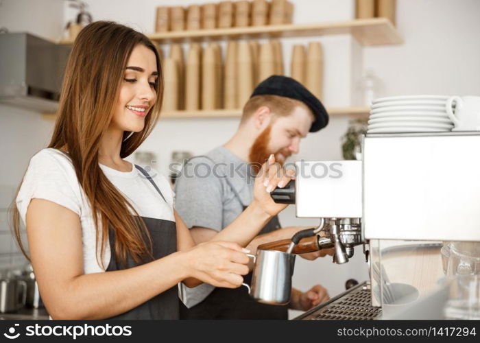 Coffee Business Concept - portrait of lady barista in apron preparing and steaming milk for coffee order with her partner while standing at cafe.