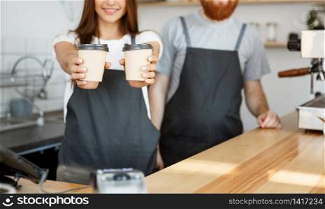 Coffee Business Concept - Positive young bearded man and beautiful attractive lady barista couple giving take away cup of coffee to custome at the modern coffee shop