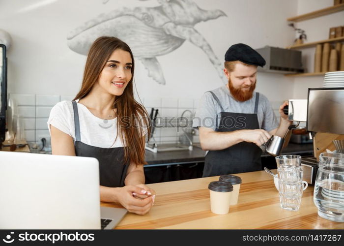 Coffee Business Concept - Positive young bearded man and beautiful attractive lady barista couple enjoy working together at the modern coffee shop