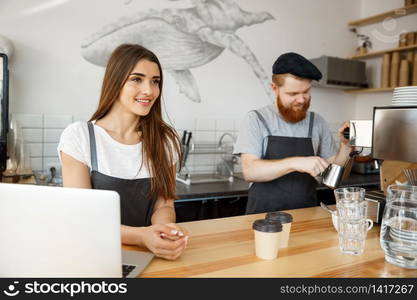 Coffee Business Concept - Positive young bearded man and beautiful attractive lady barista couple enjoy working together at the modern coffee shop