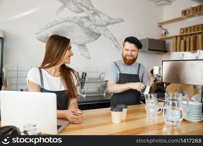 Coffee Business Concept - Positive young bearded man and beautiful attractive lady barista couple enjoy working together at the modern coffee shop