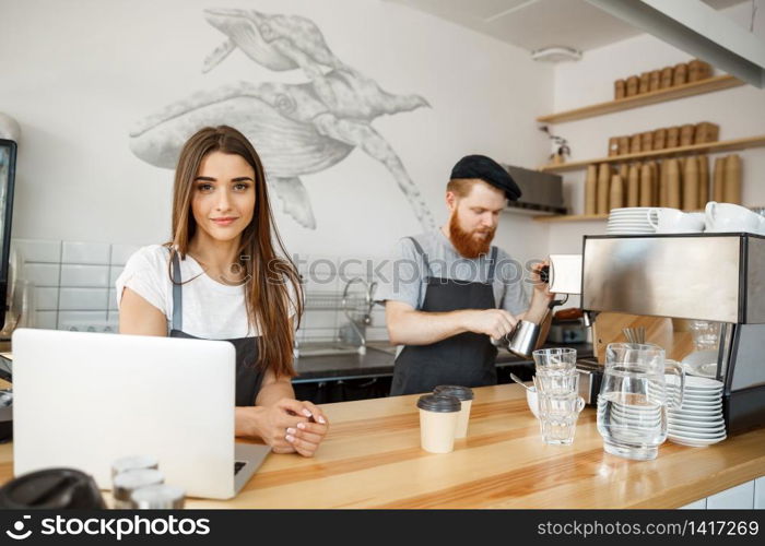 Coffee Business Concept - Positive young bearded man and beautiful attractive lady barista couple enjoy working together at the modern coffee shop