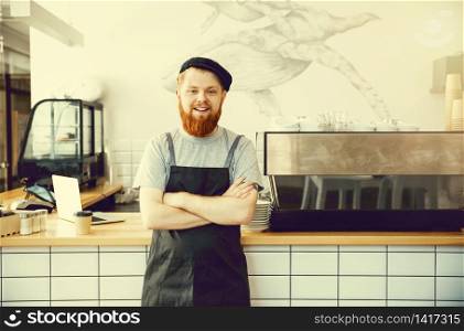 Coffee Business Concept - Positive young bearded man in apron looking at camera while standing at bar Counter.. Coffee Business Concept - Positive young bearded man in apron looking at camera while standing at bar Counter